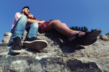 Handsome man & pregnant beautiful woman sitting on cliff, feet c