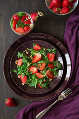 Fresh salad with strawberry, arugula and walnuts on purple plate. Low key