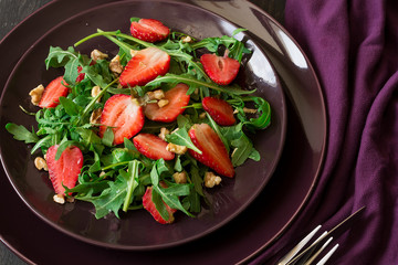 Fresh salad with strawberry, arugula and walnuts on purple plate. Low key
