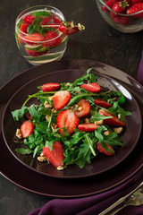 Fresh salad with strawberry, arugula and walnuts on purple plate. Low key