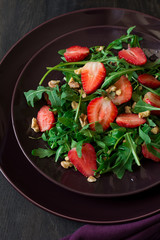 Fresh salad with strawberry, arugula and walnuts on purple plate. Low key