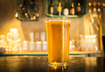 Glass of light beer on a dark pub.