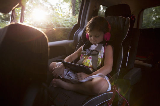 Girl wearing headphones using digital tablet in car back seat