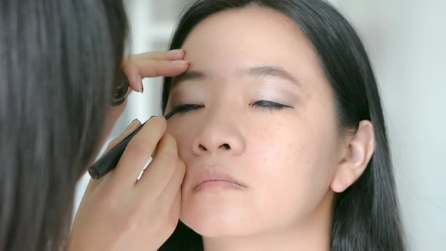 Woman is doing facial cosmetic makeup using eyeliner pencil to a model in HD quality
