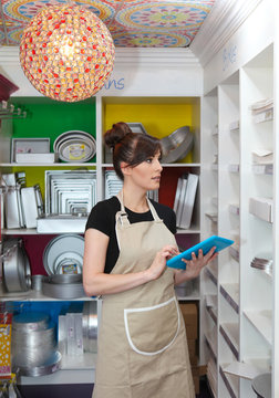 Young woman working in cake shop, holding digital tablet, counting stock