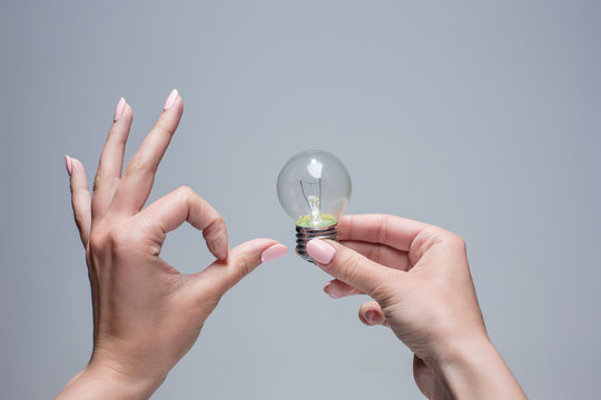 Hand holding an incandescent light bulb on gray background