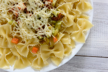 Pasta farfalle with slices of vegetables on a wooden background.