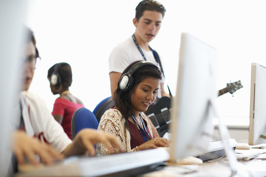 Female college student wearing headphones playing keyboards looking down smiling