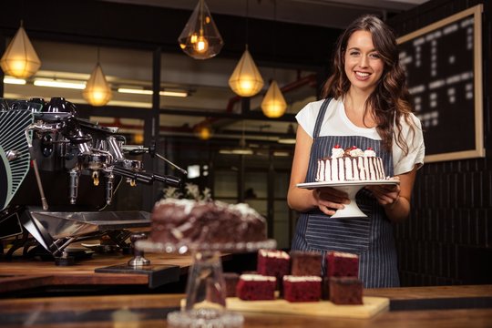 Smiling barista holding plate with cake