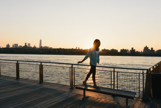 Mid adult woman balancing on bench at city waterfront at sunset