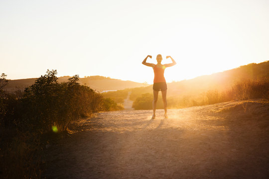 Female jogger flexing arms in sunlight, Poway, CA, USA