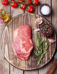 Raw fresh meat Steak with salt and pepper, rosemary and tomatoes on cutting board on dark wooden background Top view