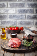 Raw fresh meat Steak with salt and pepper, rosemary and tomatoes on cutting board on dark wooden background Copy space.