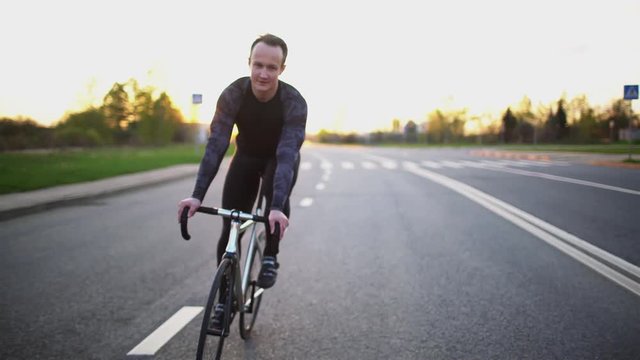 Man riding fixed gear bike on the road at sunset in slow motion