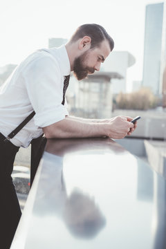 Stylish businessman reading smartphone text leaning against office balcony