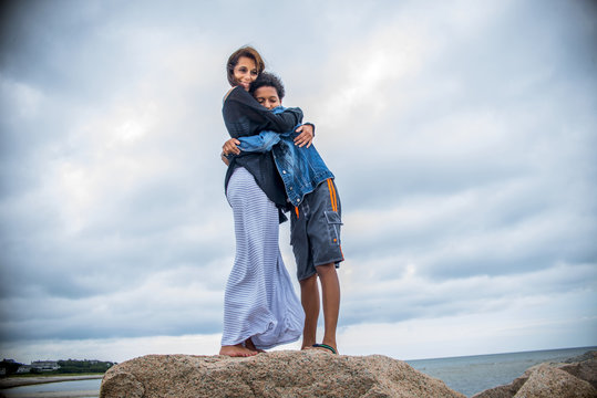 Portrait of mature woman and son hugging on coastal rocks, Cape Cod, USA