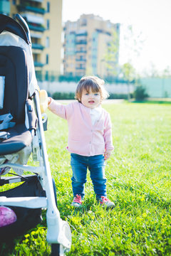 Female toddler holding onto pushchair in park