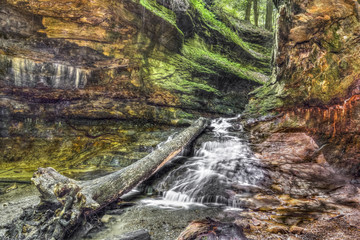 Water cascades over colorful sandstone from a narrow passage with green rocky walls In Indiana's Turkey Run State Park.