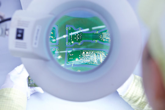 Young woman using magnifier at quality check station at factory producing flexible electronic circuit boards. Plant is located in the south of China, in Zhuhai, Guangdong province