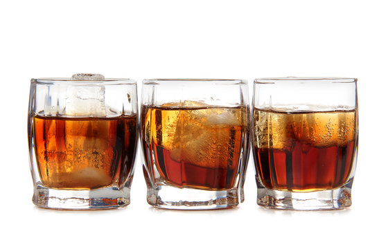 Glass jars with whiskey and ice on white background