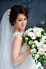 Naklejka premium Beauty bride in bridal gown with bouquet and lace veil indoors. Beautiful model girl in a white wedding dress. Female portrait of cute lady. Woman with hairstyle
