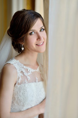 Fototapeta premium Beauty bride in bridal gown with lace veil indoors. Beautiful model girl in a white wedding dress. Female portrait of cute lady. Woman with hairstyle