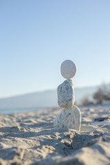 Sculpture made with stack stones in equilibrium close to the shore on a sandy beach.