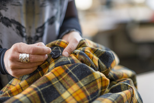 Close up seamstress hand sewing button onto tartan jacket in workshop