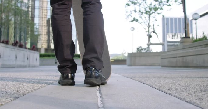 Close view of young man's smart shoes as he flips up a skateboard and turns towards camera in Downtown Los Angeles.  Slow motion recorded at 60fps.