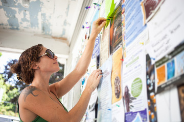 Mid adult woman pinning up notice on community notice board
