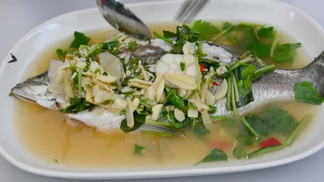 A person eating spicy steamed seabass lemon soup with herbs and vegetable in white dish serve in the restaurant as Thai cuisine food in HD 