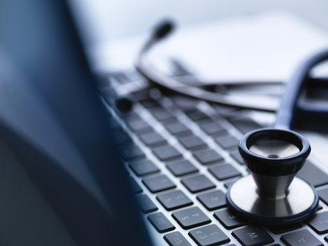 Close up of stethoscope on top of laptop computer keyboard on doctors desk