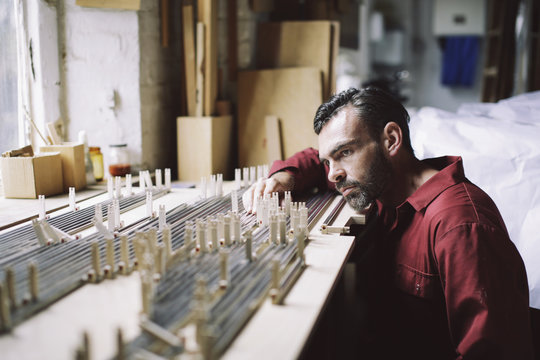 Mature craftsman checking organ pipes in pipe organ workshop