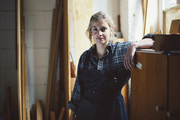 Portrait of young craftswoman leaning on cupboard in organ workshop