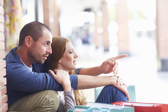 Couple sitting by shopping bags, man pointing