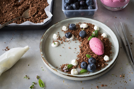 Mixed berry  mousse served on chocolate soil with cream drops, blueberries, lemon balm leaves and thyme flowers. Concept of food plating in modern nordic style. Selective focus.