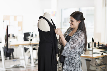 Young seamstress fitting dress on tailors dummy in workshop