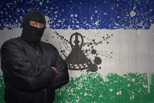 dangerous man in a mask standing near a wall with painted national flag of lesotho