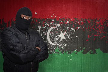 dangerous man in a mask standing near a wall with painted national flag of libya