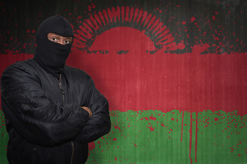 dangerous man in a mask standing near a wall with painted national flag of malawi