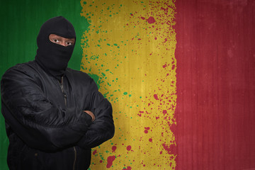 dangerous man in a mask standing near a wall with painted national flag of mali