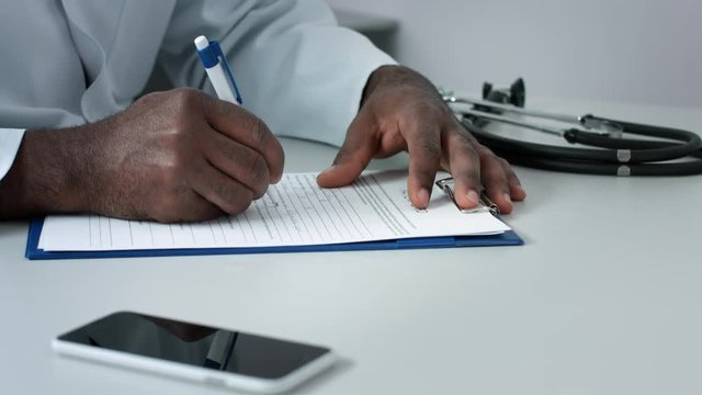 Dark-skinned male doctor filling patient chart