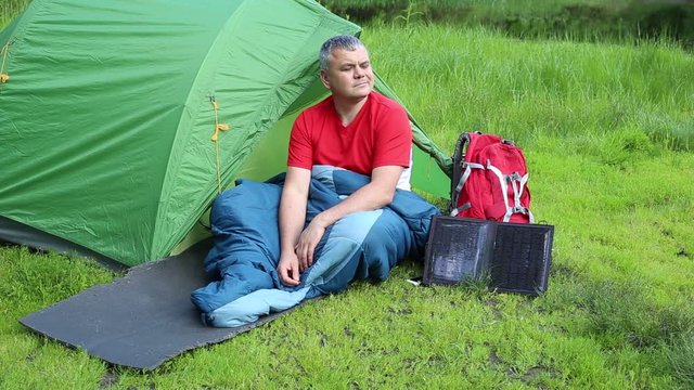 A man sitting near tent and talking on the phone.
