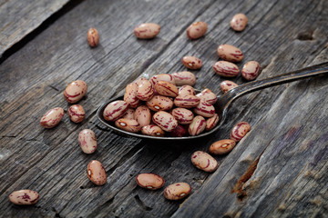 Cranberry beans on spoon, on wooden surface.