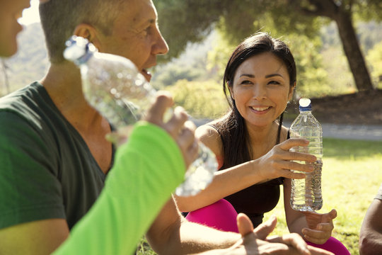 Mature Male And Female Runners Taking A Water Break In Park