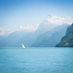 Naklejka premium Grandiose mountain landscape. Mountain tops in the snow. White sail on a romantic lake.