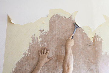 Mature man using scraper to scrape off old wallpaper