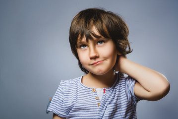 Closeup Thoughtful Young Boy Looking Up with Hand on Face Against Gray Background