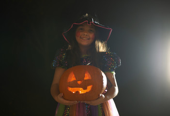 Portrait of girl wearing halloween witch costume holding pumpkin