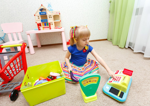 Little blond girl playing role game with toy cash register